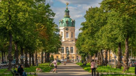 Das Schloss Charlottenburg an einem sonnigen Tag, diverse Menschen die spazieren und auf B&auml;nken sitzen