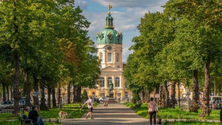 Das Schloss Charlottenburg an einem sonnigen Tag, diverse Menschen die spazieren und auf B&auml;nken sitzen