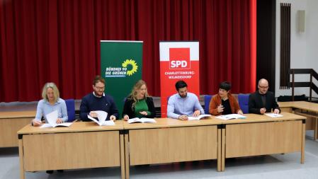 6 Personen sitzen an einem Tisch und unterzeichnen ein Papier